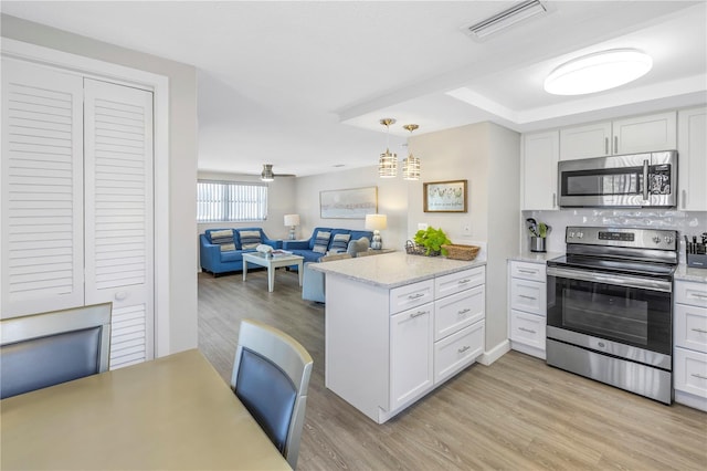 kitchen featuring white cabinets, hanging light fixtures, light hardwood / wood-style flooring, light stone counters, and stainless steel appliances