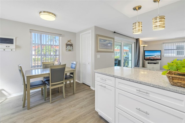 kitchen featuring white cabinets, decorative light fixtures, light hardwood / wood-style floors, and light stone countertops