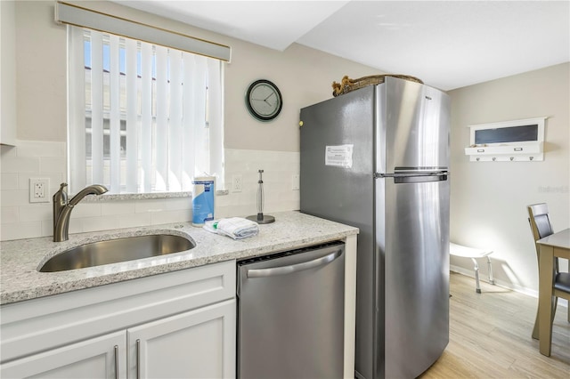 kitchen with appliances with stainless steel finishes, tasteful backsplash, light stone counters, sink, and white cabinetry