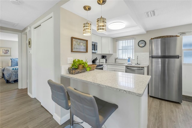 kitchen with kitchen peninsula, appliances with stainless steel finishes, a kitchen breakfast bar, pendant lighting, and white cabinets