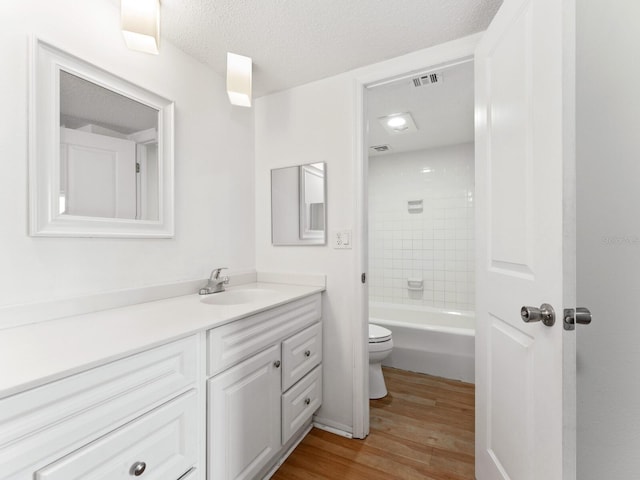 full bathroom featuring vanity, a textured ceiling, hardwood / wood-style flooring, toilet, and tiled shower / bath