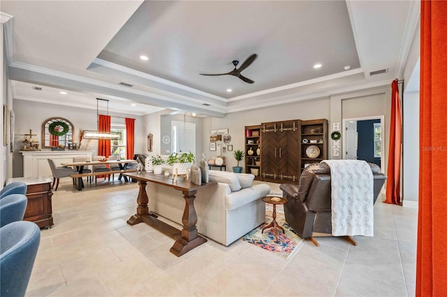 tiled living room with ornamental molding, ceiling fan, and a tray ceiling