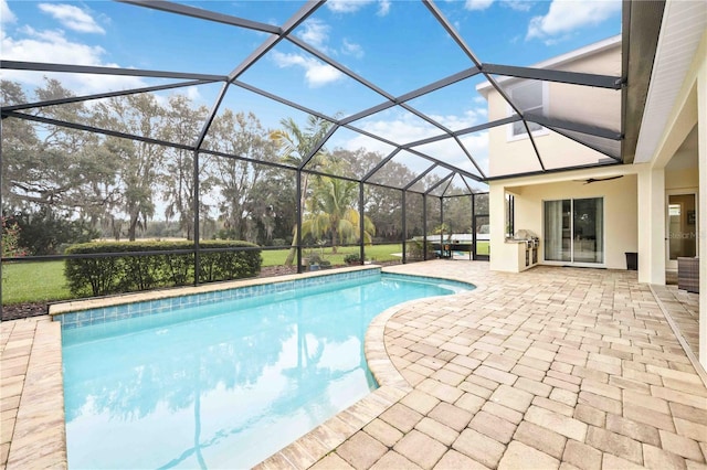 view of swimming pool featuring a patio area, exterior kitchen, ceiling fan, and glass enclosure