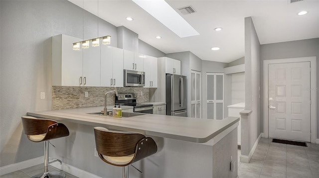 kitchen with kitchen peninsula, white cabinetry, a kitchen bar, appliances with stainless steel finishes, and lofted ceiling with skylight