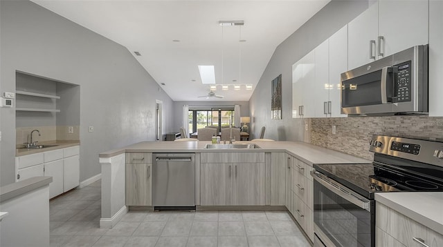 kitchen featuring light tile floors, vaulted ceiling with skylight, kitchen peninsula, and stainless steel appliances