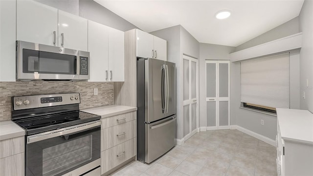 kitchen featuring white cabinets, appliances with stainless steel finishes, backsplash, light tile flooring, and lofted ceiling