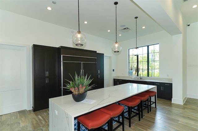 kitchen with pendant lighting, sink, a kitchen island, light stone counters, and a kitchen bar