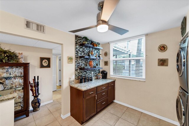 kitchen with ceiling fan, light stone counters, stacked washer / dryer, and light tile patterned flooring