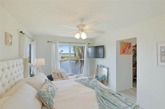 bedroom with light wood-type flooring, a textured ceiling, a spacious closet, and ceiling fan