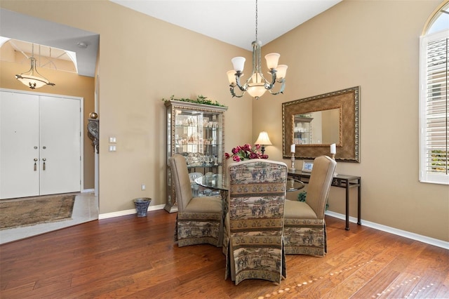 dining area with hardwood / wood-style flooring, vaulted ceiling, and an inviting chandelier