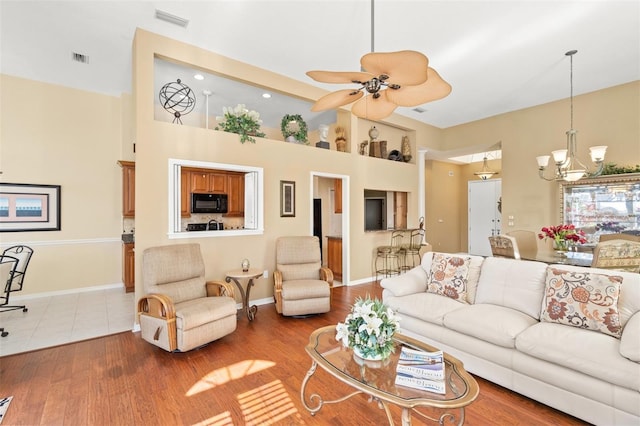 living room featuring wood-type flooring, ceiling fan with notable chandelier, and a high ceiling