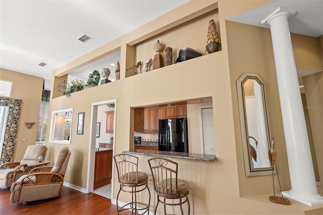 kitchen featuring a breakfast bar, dark stone countertops, black refrigerator with ice dispenser, decorative columns, and dark hardwood / wood-style flooring