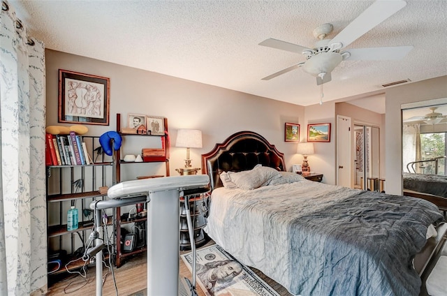 bedroom with a textured ceiling, wood-type flooring, and ceiling fan