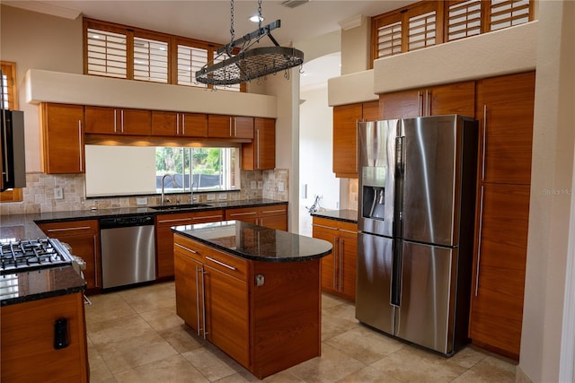 kitchen with sink, a center island, appliances with stainless steel finishes, dark stone counters, and backsplash