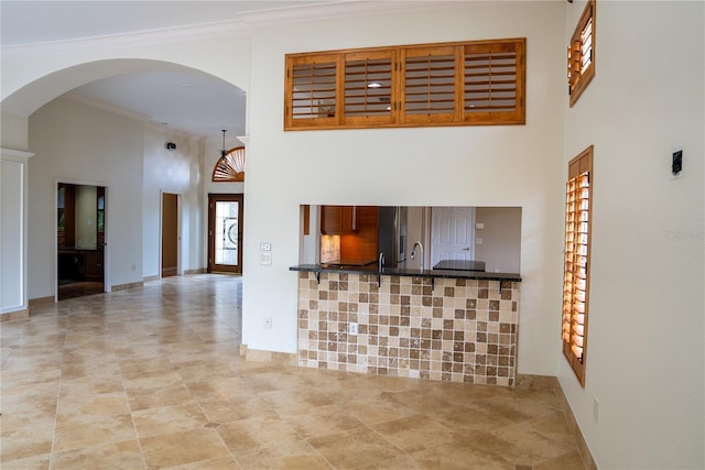 unfurnished living room featuring ornamental molding, sink, and a high ceiling