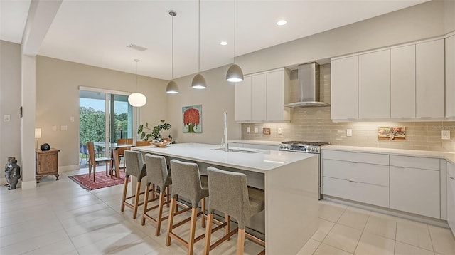 kitchen with a center island with sink, wall chimney exhaust hood, white cabinetry, and backsplash