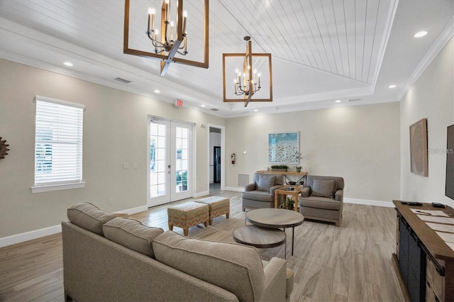 living room featuring an inviting chandelier, french doors, a raised ceiling, light wood-type flooring, and ornamental molding