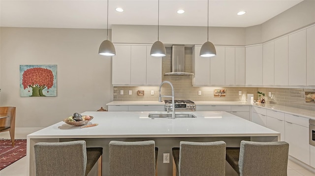 kitchen featuring a breakfast bar, wall chimney range hood, and a kitchen island with sink