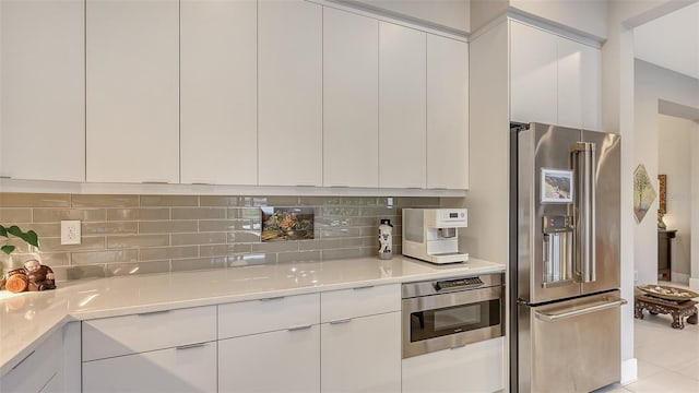 kitchen featuring tasteful backsplash, white cabinets, stainless steel appliances, and light tile patterned floors