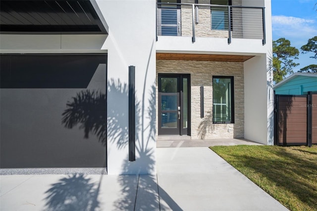 entrance to property with stone siding, a lawn, a balcony, and stucco siding