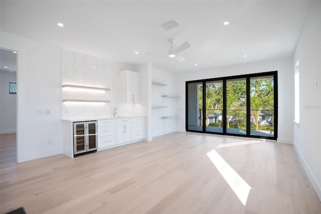 unfurnished living room with beverage cooler, baseboards, light wood-style flooring, and recessed lighting