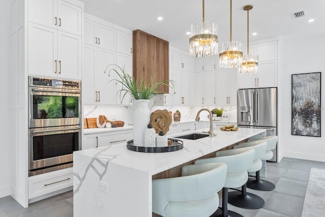 kitchen with stainless steel appliances, a sink, a kitchen island with sink, and white cabinetry