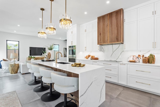 kitchen featuring a kitchen island with sink, a sink, white cabinetry, open floor plan, and pendant lighting