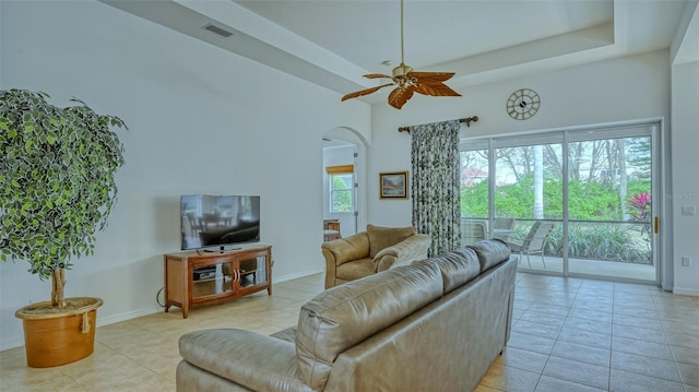 living room with a raised ceiling, ceiling fan, and light tile patterned flooring