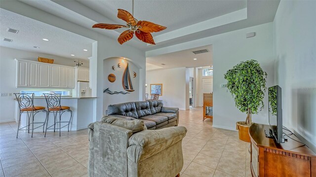 tiled living room with a raised ceiling and ceiling fan