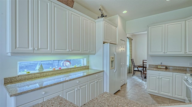 kitchen with light stone countertops, white cabinetry, light tile patterned floors, and white refrigerator with ice dispenser