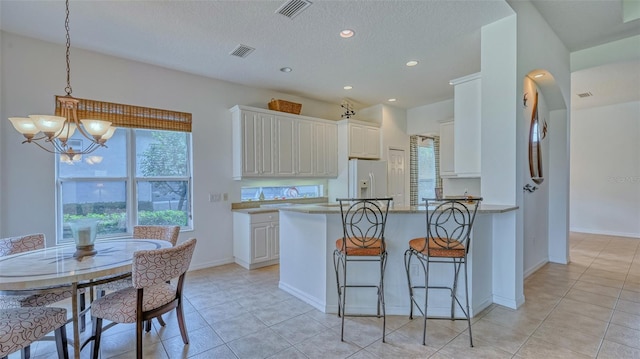 kitchen featuring white fridge with ice dispenser, light tile patterned floors, a notable chandelier, pendant lighting, and white cabinets