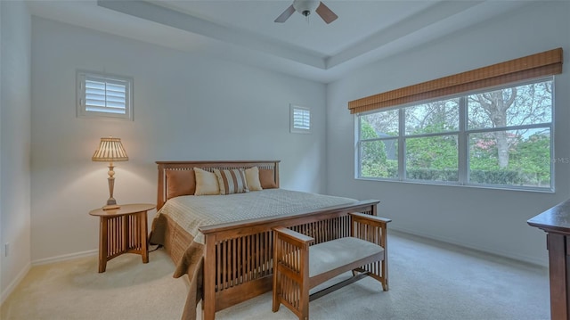 bedroom with a tray ceiling, baseboards, light colored carpet, and ceiling fan