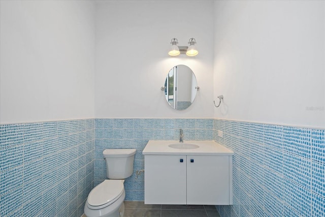 bathroom featuring toilet, vanity, tile patterned flooring, and tile walls