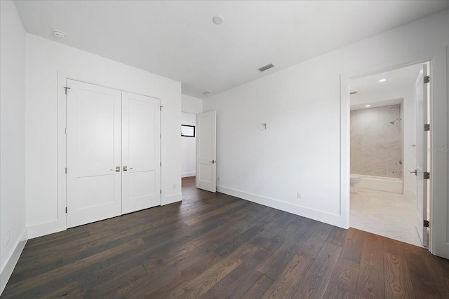 unfurnished bedroom featuring dark wood-type flooring, a closet, and ensuite bath