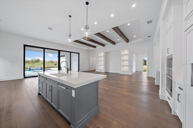 kitchen featuring gray cabinetry, a kitchen island with sink, light stone countertops, beam ceiling, and sink