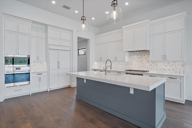 kitchen featuring dark hardwood / wood-style floors, white cabinetry, a center island with sink, and decorative light fixtures