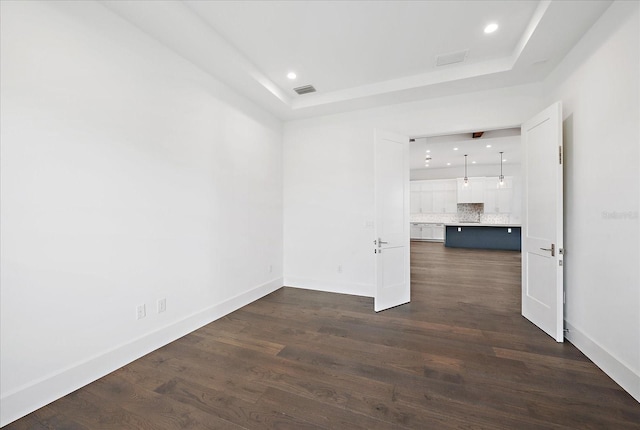 empty room featuring a raised ceiling and dark hardwood / wood-style flooring