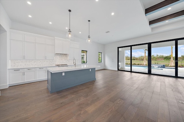 kitchen with dark hardwood / wood-style floors, pendant lighting, sink, a kitchen island with sink, and white cabinets