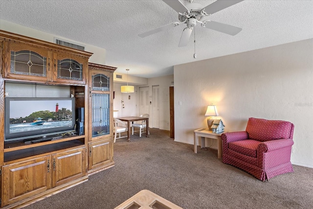 living area featuring dark carpet, ceiling fan, and a textured ceiling