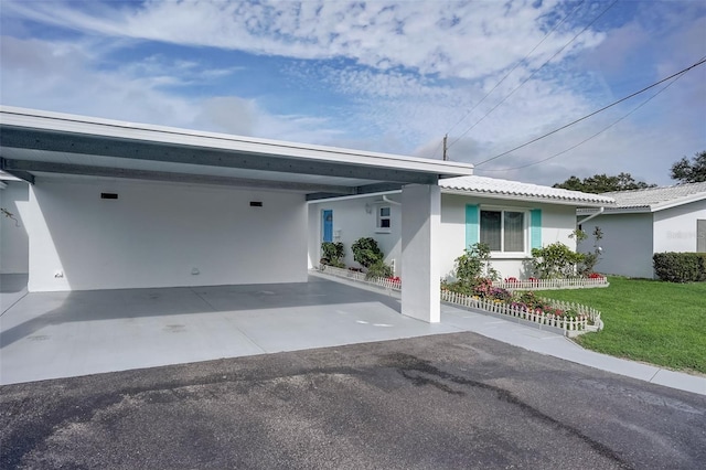 ranch-style house featuring driveway, an attached carport, a front lawn, and stucco siding