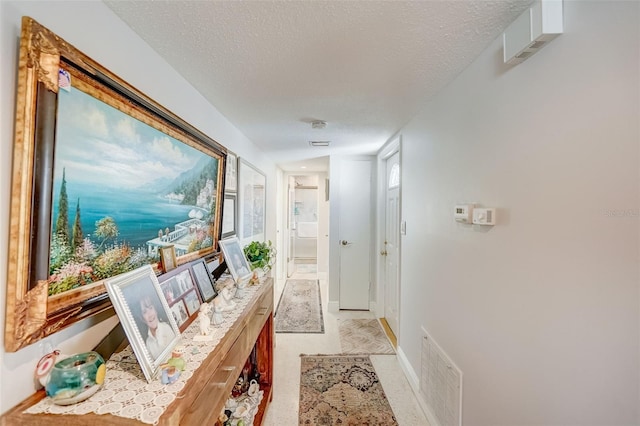 hallway with a textured ceiling, visible vents, and baseboards