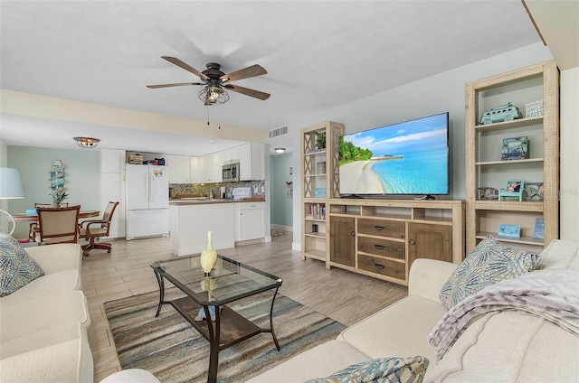 living room with a textured ceiling, ceiling fan, and light hardwood / wood-style flooring