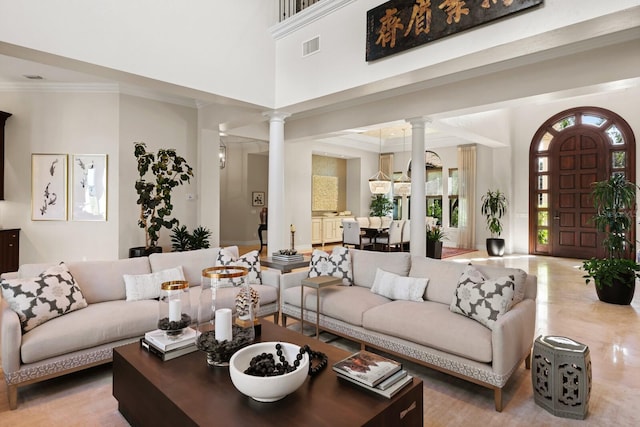 living room with decorative columns, ornamental molding, a towering ceiling, and a wealth of natural light