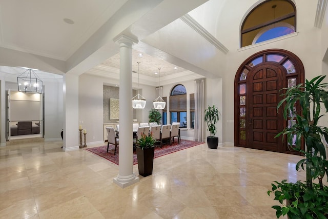 entryway featuring ornate columns, ornamental molding, a high ceiling, and an inviting chandelier