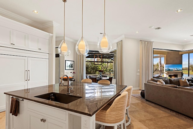 kitchen featuring pendant lighting, sink, white cabinetry, a kitchen island with sink, and dark stone counters