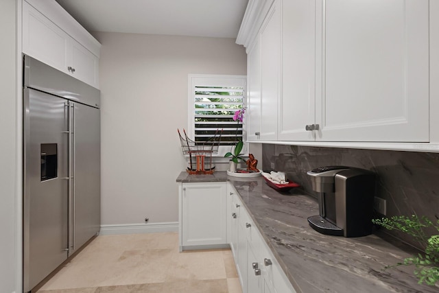 kitchen featuring white cabinetry, stainless steel built in fridge, light stone counters, and decorative backsplash