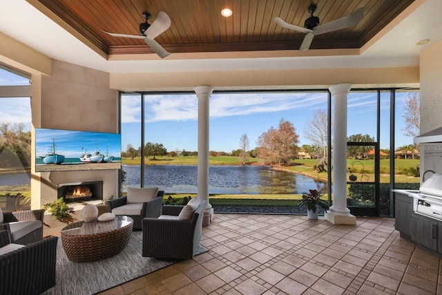 sunroom featuring a water view, wood ceiling, an outdoor fireplace, a raised ceiling, and ceiling fan