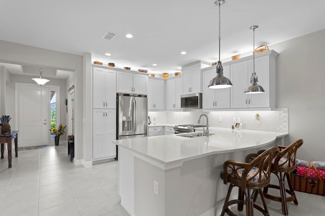 kitchen with appliances with stainless steel finishes, hanging light fixtures, a breakfast bar, kitchen peninsula, and sink