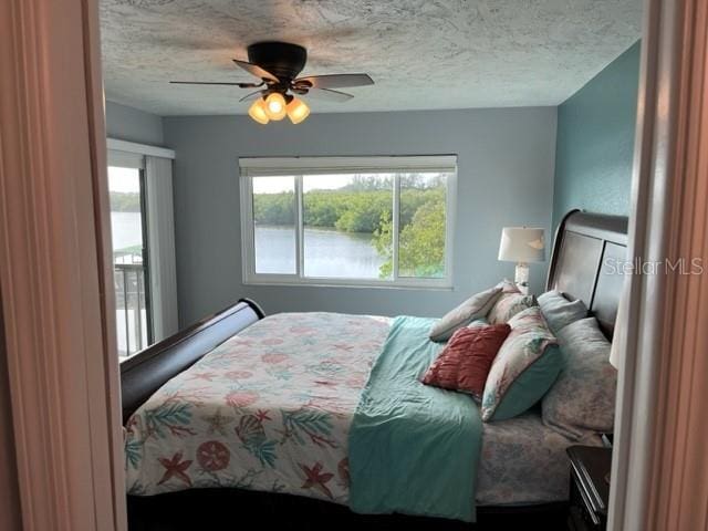 bedroom with a water view, ceiling fan, and a textured ceiling