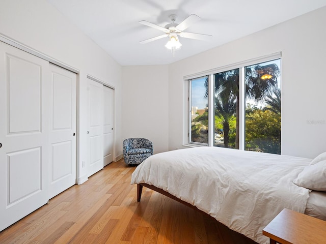 bedroom featuring two closets, light hardwood / wood-style floors, and ceiling fan